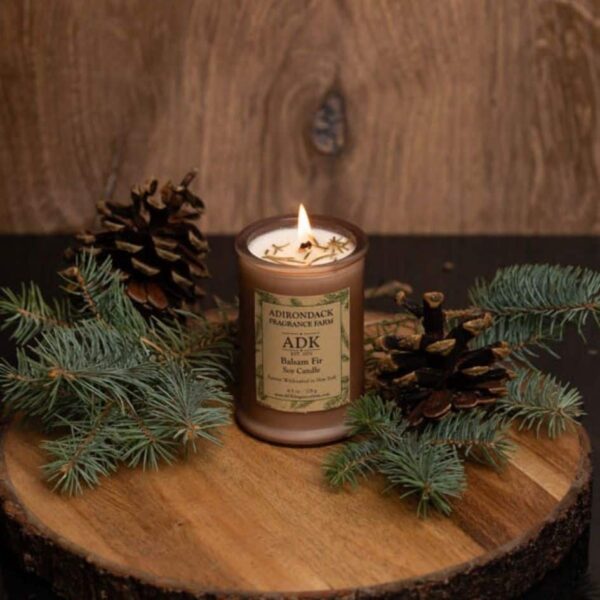 Balsam Fir Candle with an ADK Label on a wooden plate and lit flame