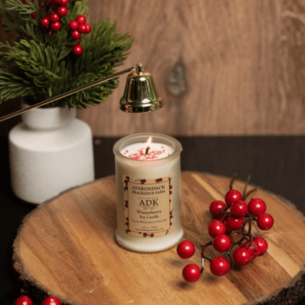 White frosted candle against a wooden background with winter berry branches