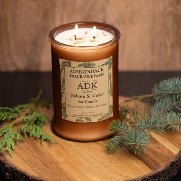 Balsam Cedar Candle with ADK label 20oz on a wooden plate lit