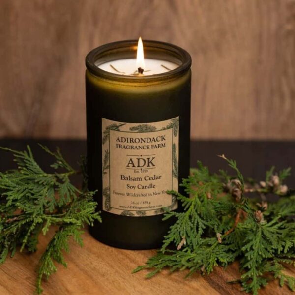 Balsam Cedar Candle 16oz with ADK Label on a wooden plate with lit flame