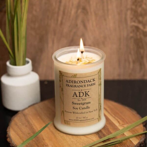 Sweetgrass Candle 20oz lit with ADK label on a wooden plate