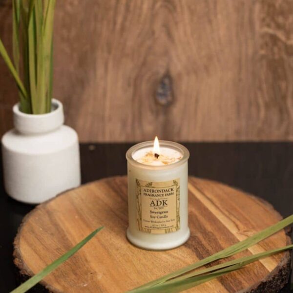 Sweetgrass Candle 4.5oz lit with ADK label on a wooden plate